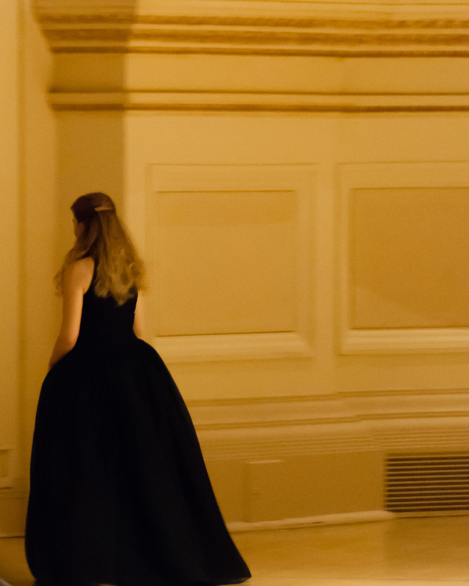 Katya Grineva walking away down a cream Carnegie Hall corridor in a black gown