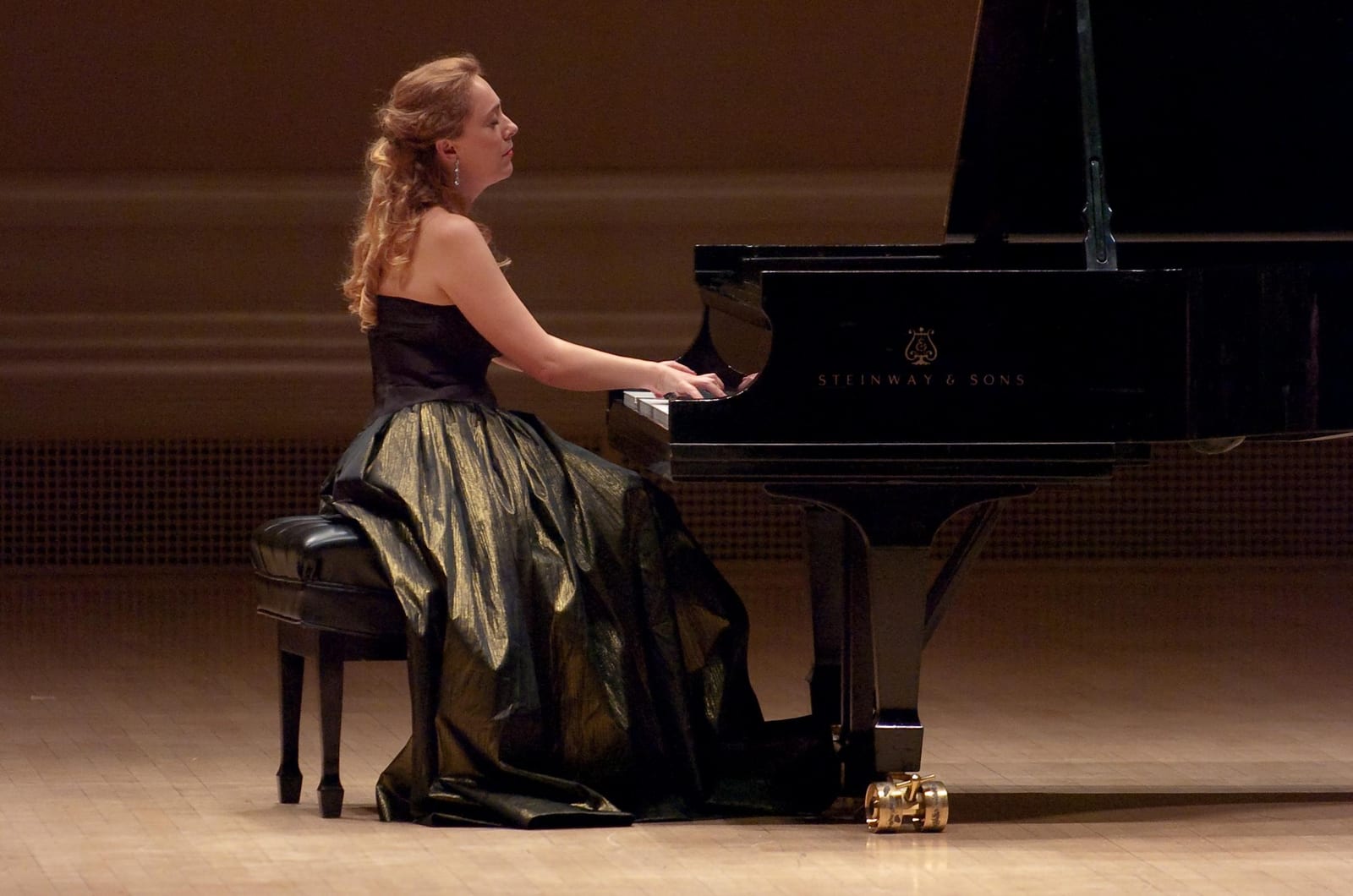 Katya Grineva in an olive satin gown at the Steinway, seen across the width of the stage