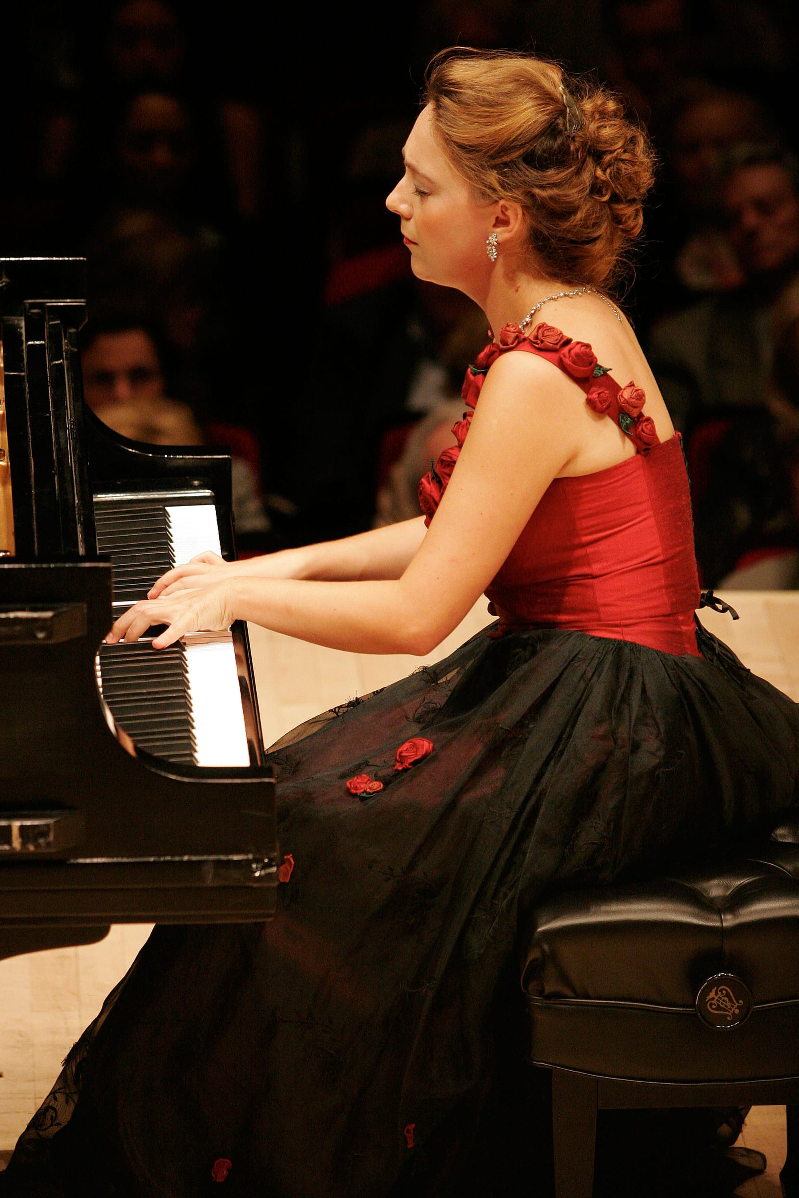 Katya Grineva playing in a black gown strapped with red roses, the audience blurred behind her