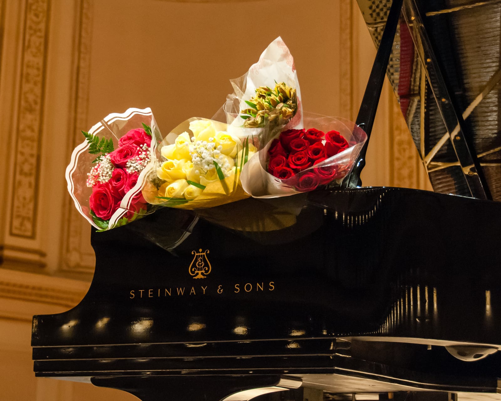 Three wrapped bouquets of red and yellow flowers resting on the closed Steinway lid