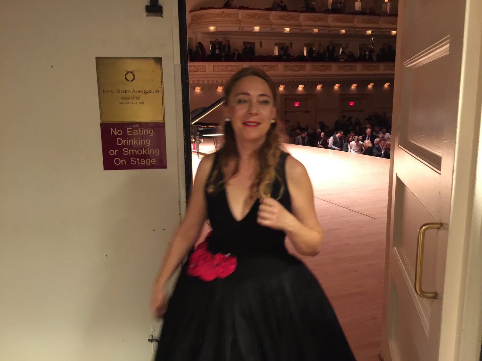 Katya Grineva smiling in the backstage doorway, a red flower at the waist of her black gown