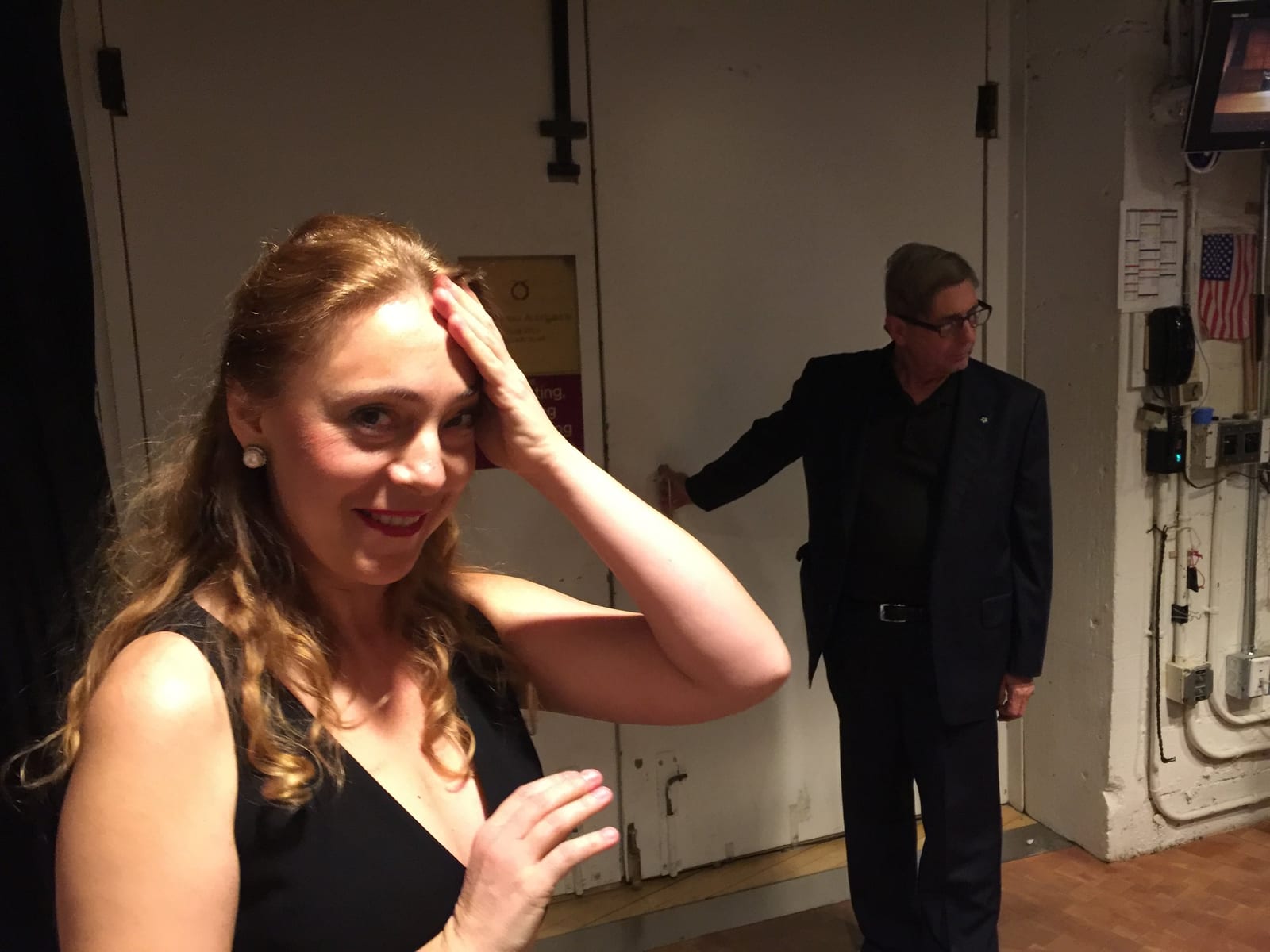 Backstage, Katya Grineva laughing with a hand in her hair while a man passes behind her