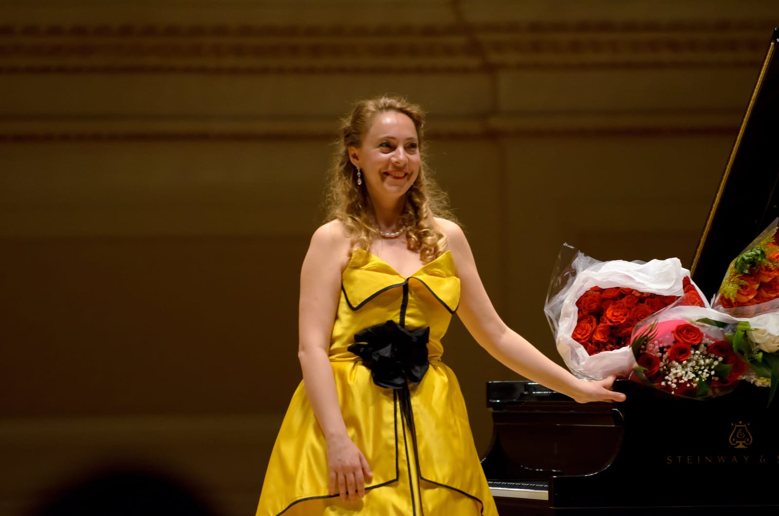 Katya Grineva in the yellow gown beside the piano, red roses lying across the lid