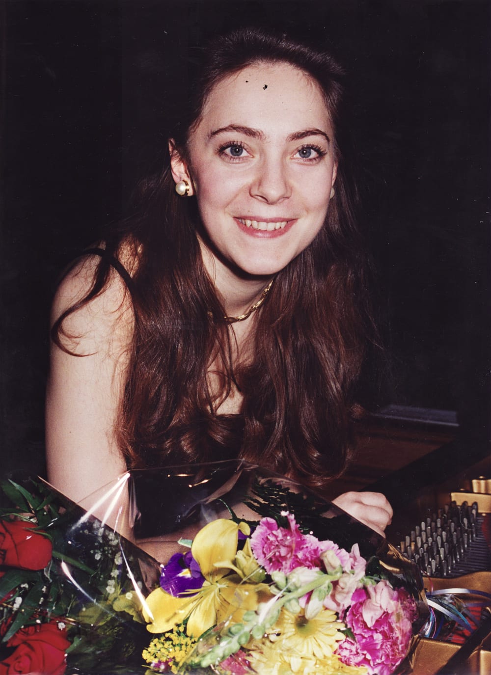 An early frame, Katya Grineva smiling behind bouquets at the piano