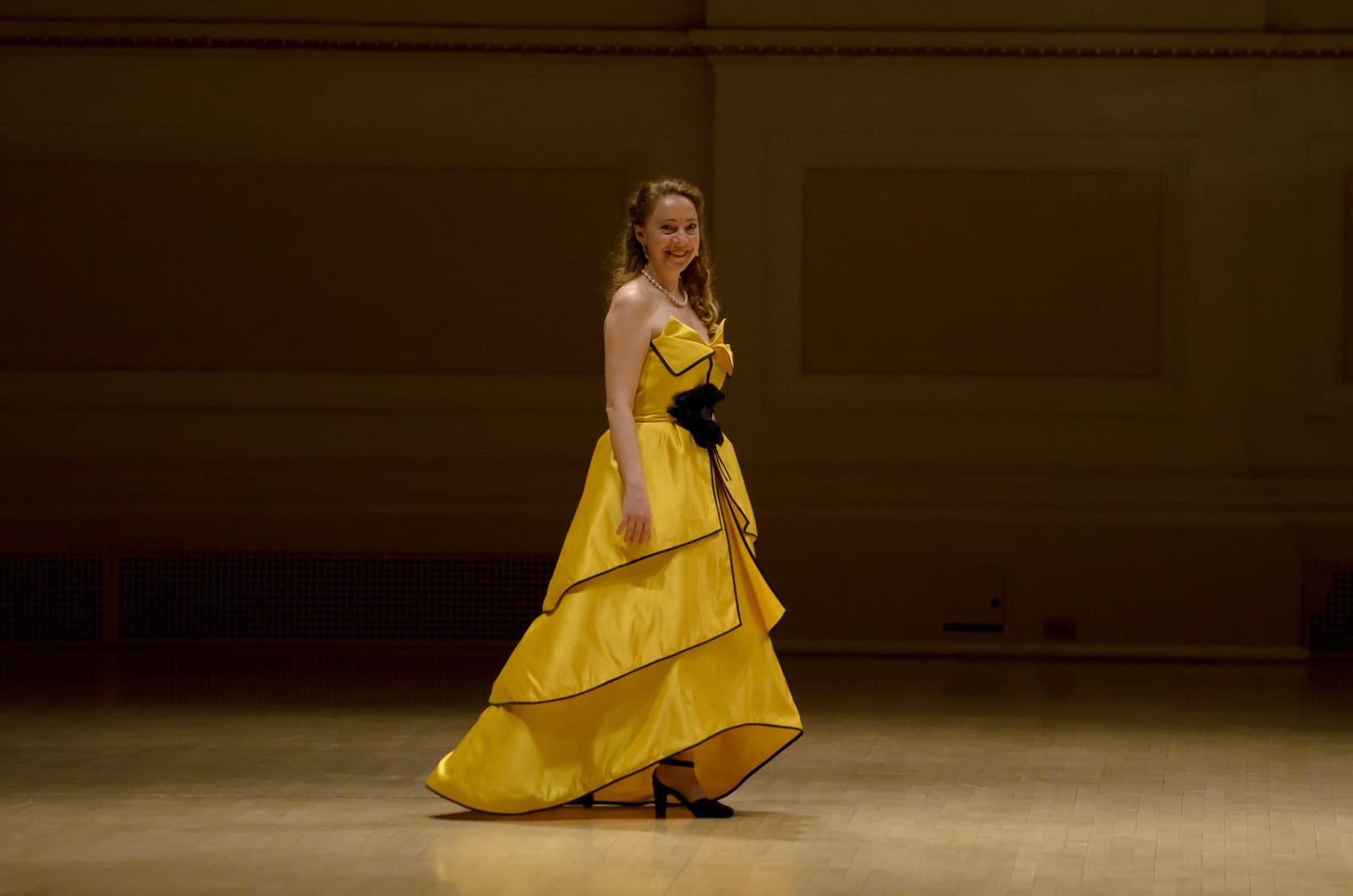 Katya Grineva in the yellow gown walking across the empty stage